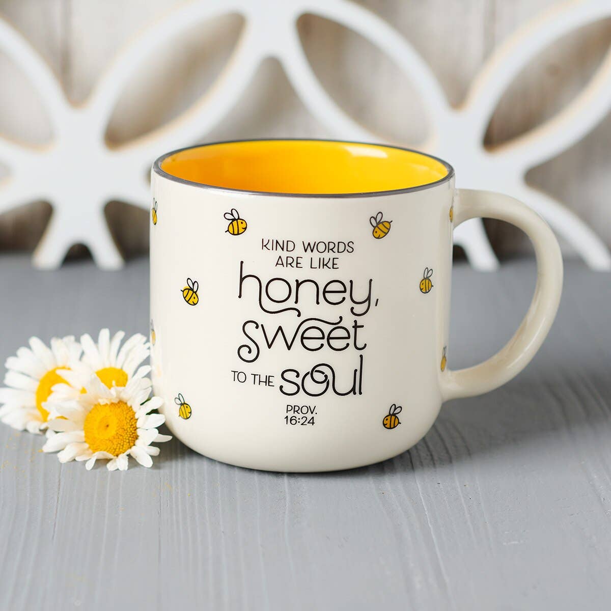 Mug with motivational quote and bee design on a wooden surface with flowers.
