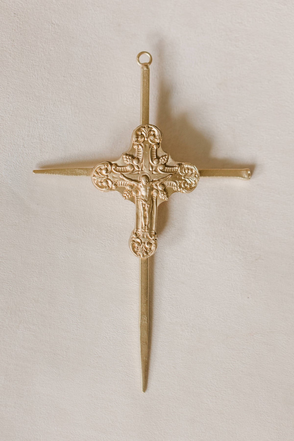 Gold cross crucifix with a nails on a light beige background