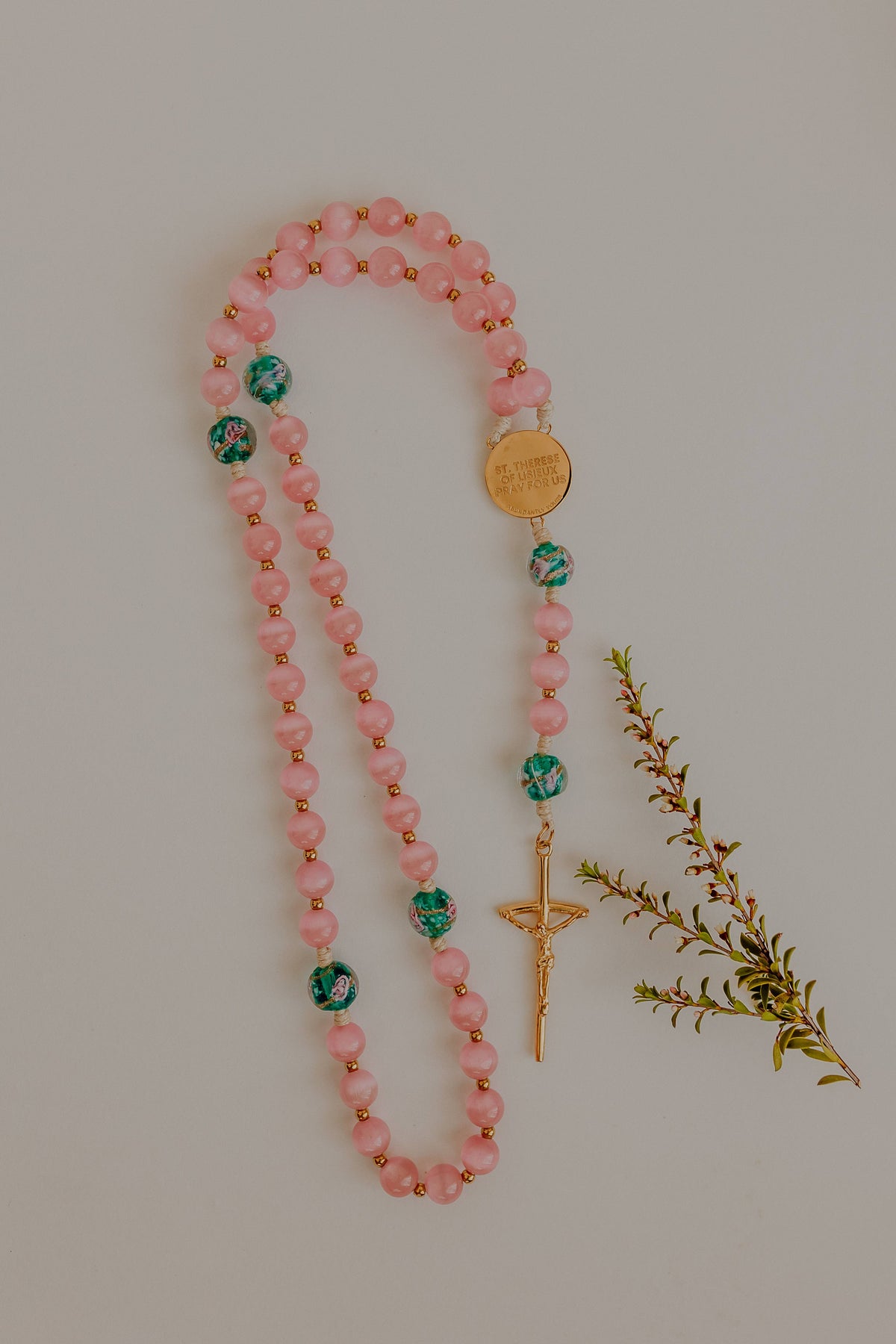 Pink beaded rosary with gold accents on a light gray background