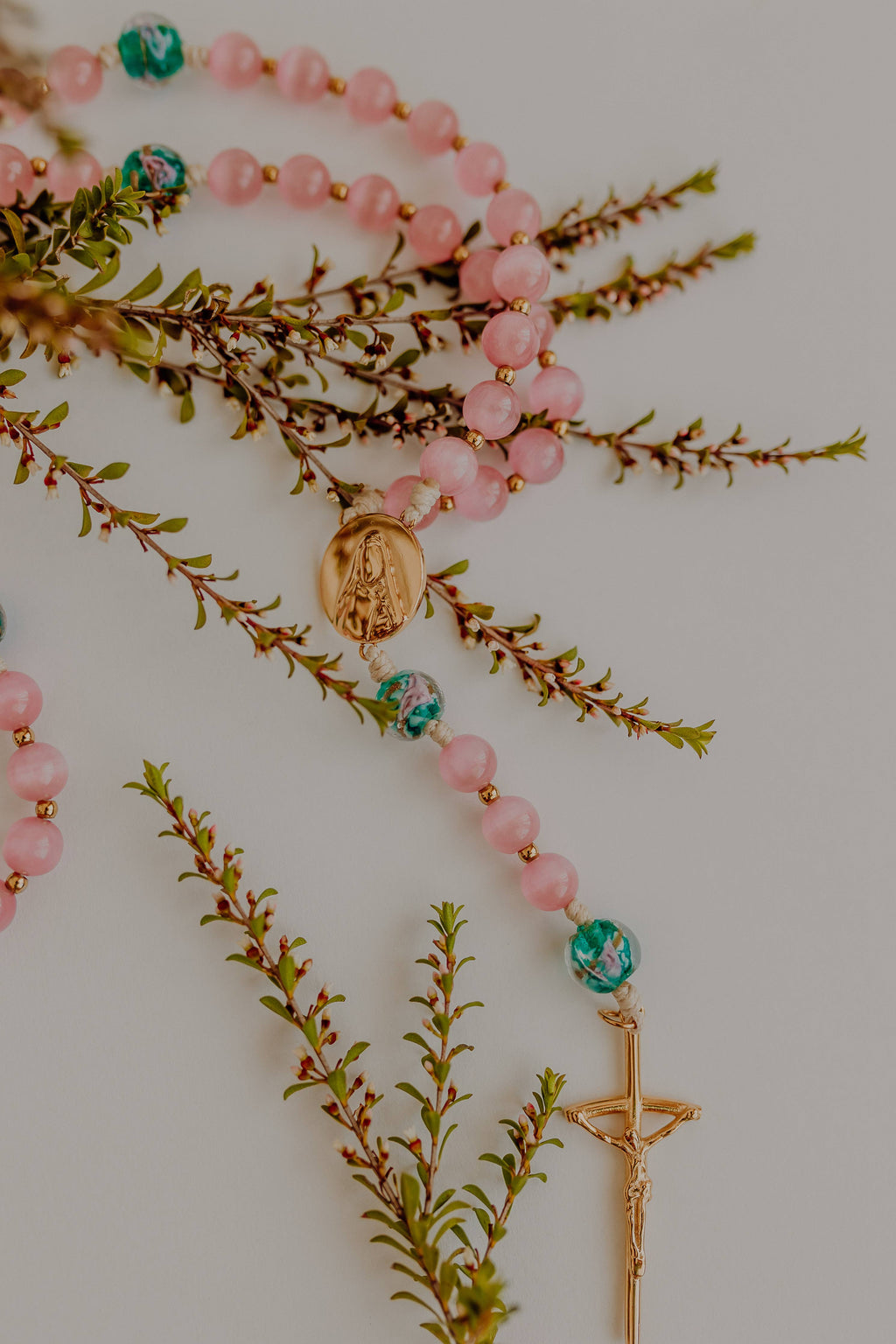 Pink beaded rosary with gold accents on a white background