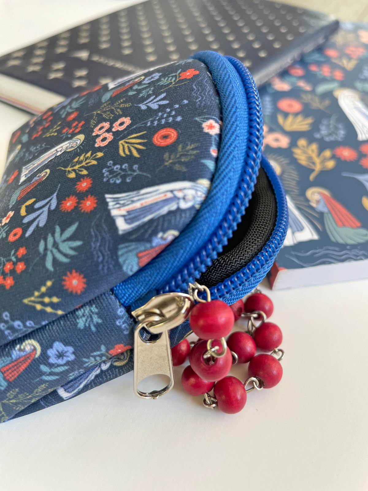 Blue floral-patterned rosary pouch with a zipper and red rosary beads on a white surface.