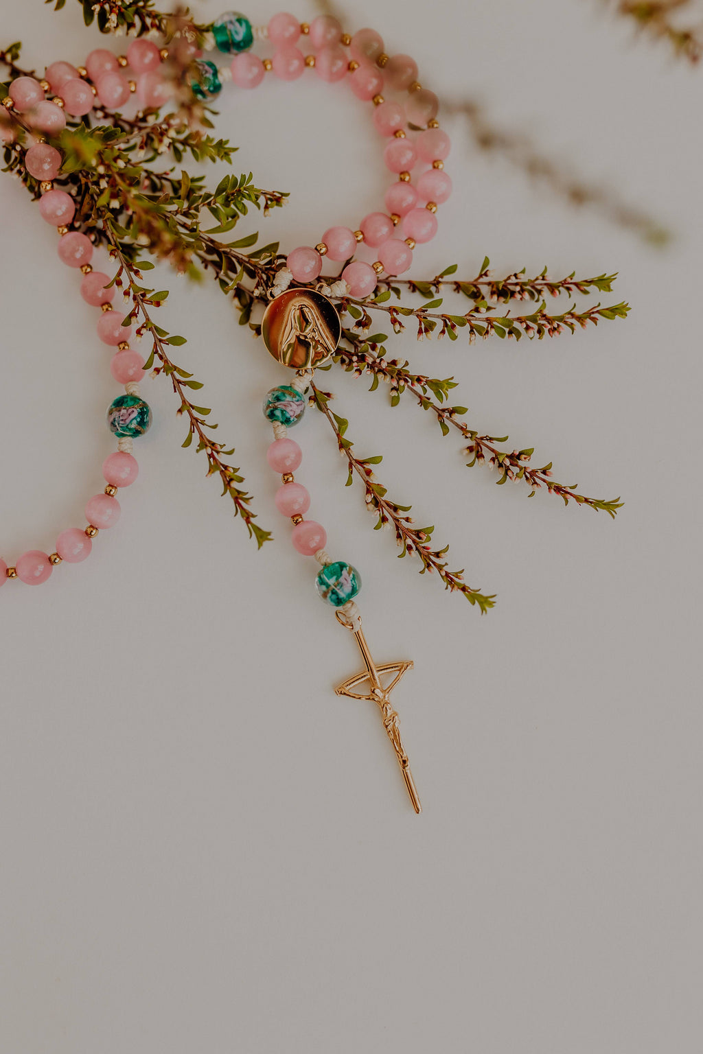 Rosary with pink beads and a gold charm on a white background