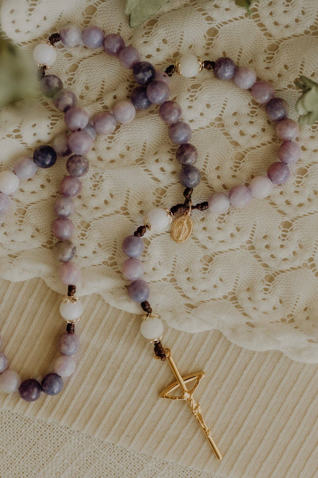 Purple and white beaded rosary with a gold cross pendant on a lace background