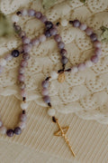 Purple and white beaded rosary with a gold cross pendant on a lace background