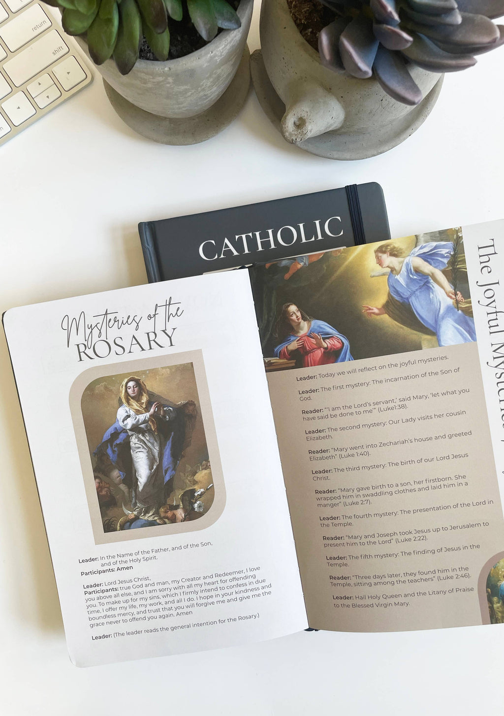 Open book on Catholic Rosary mysteries with a keyboard and plants in the background