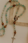Catholic rosary with turquoise and brown beads and a silver crucifix on a beige background