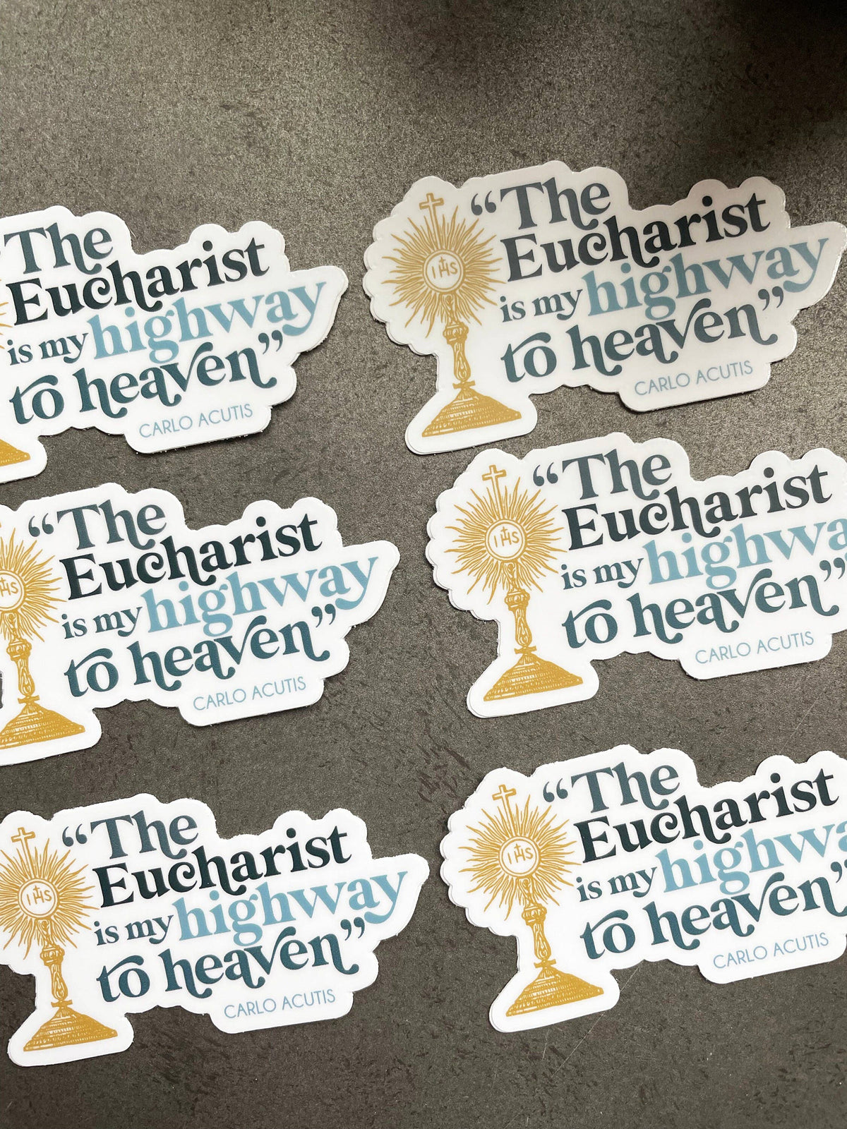 Multiple stickers with 'The Eucharist is my highway to heaven' text on a dark background
