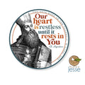 A circular printed design featuring an illustrated Saint Augustine with a long beard holding a book and candle, surrounded by the text 'Our heart is restless until it rests in You' on a white background.