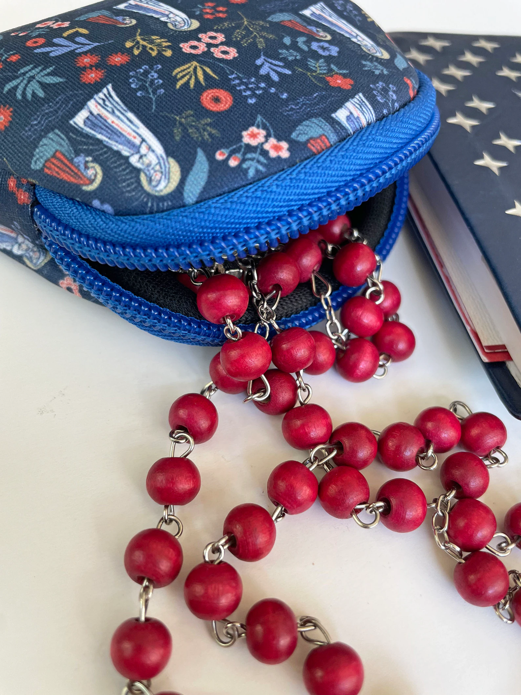 Blue patterned rosary pouch with a red beaded rosary on a white surface