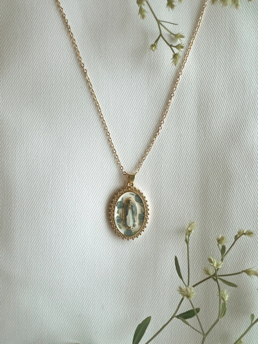 Gold necklace with a pendant on a light background with greenery