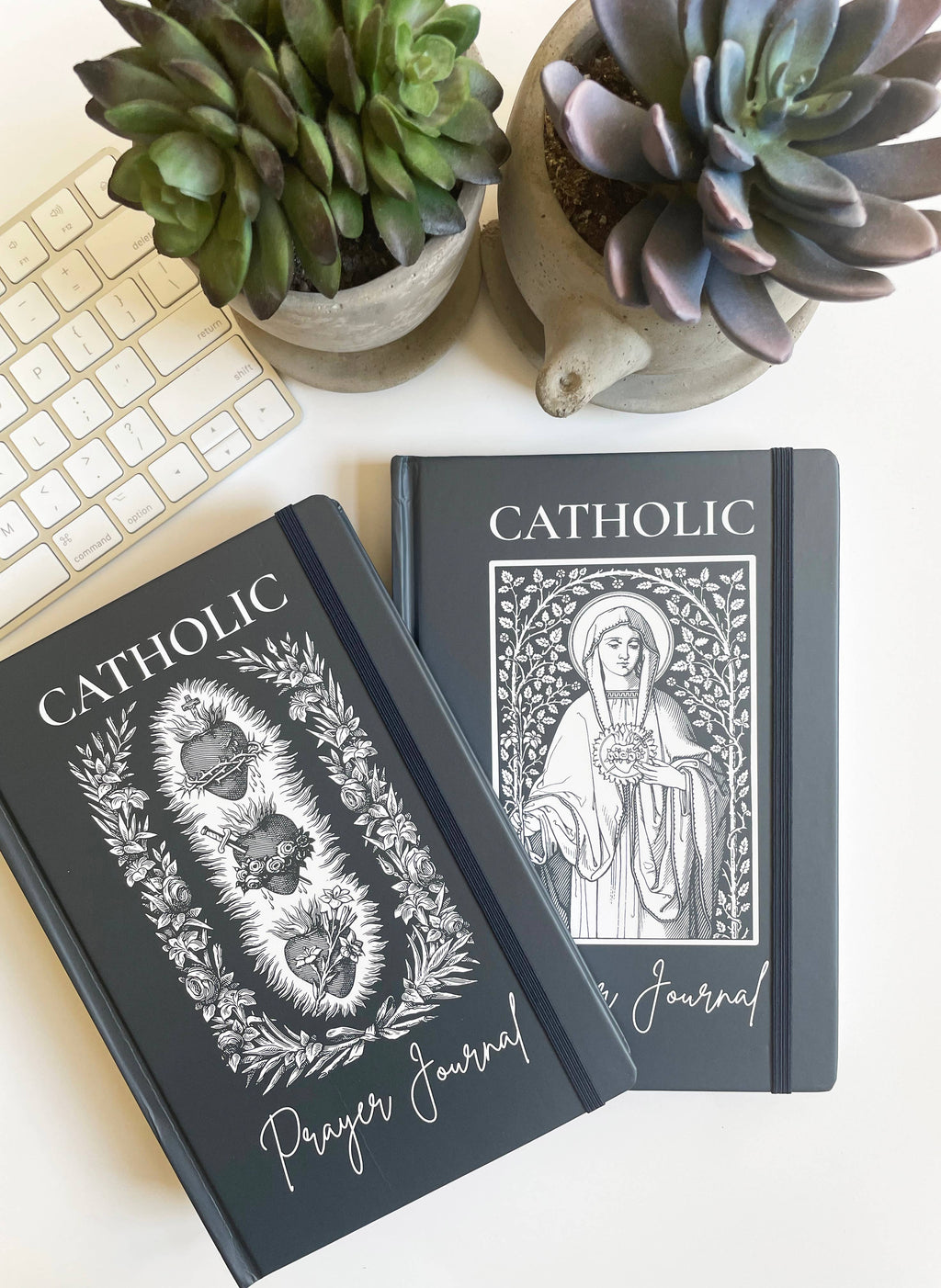 Two Catholic prayer journals on a desk with succulents in the background.