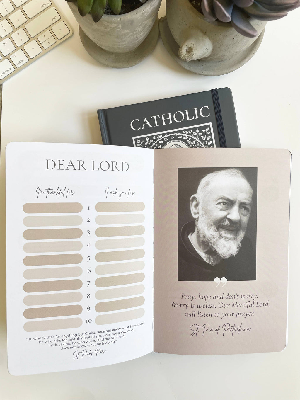Open book with a portrait of St. Padre Pio  and text on a white surface with plants and a keyboard.