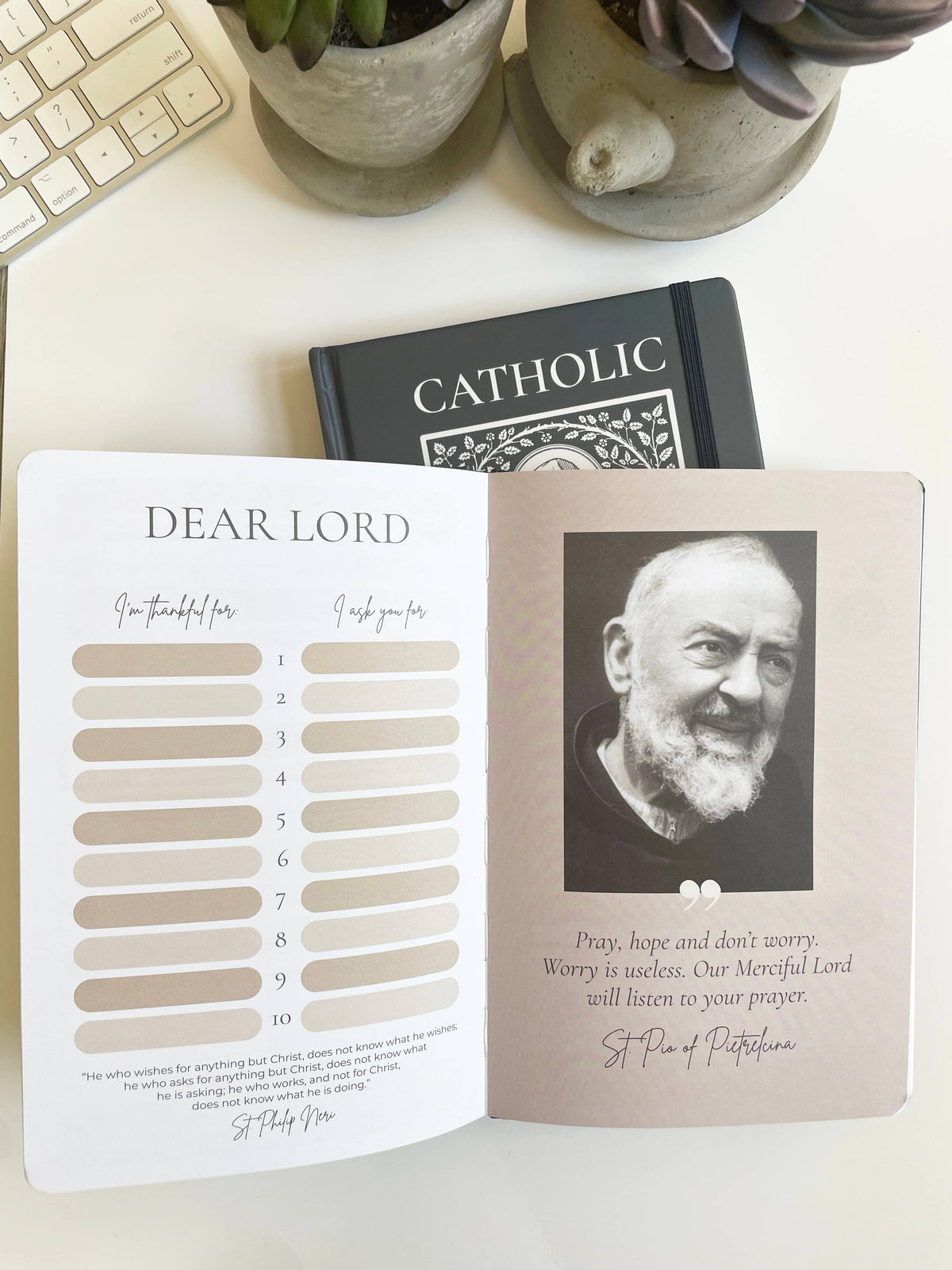 Open book with a portrait of St. Padre Pio  and text on a white surface with plants and a keyboard.