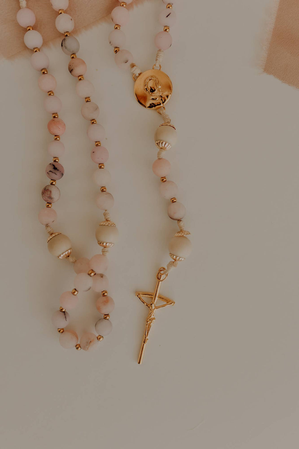 Catholic rosary with pink beads and a gold pendant and crucifix on a neutral background