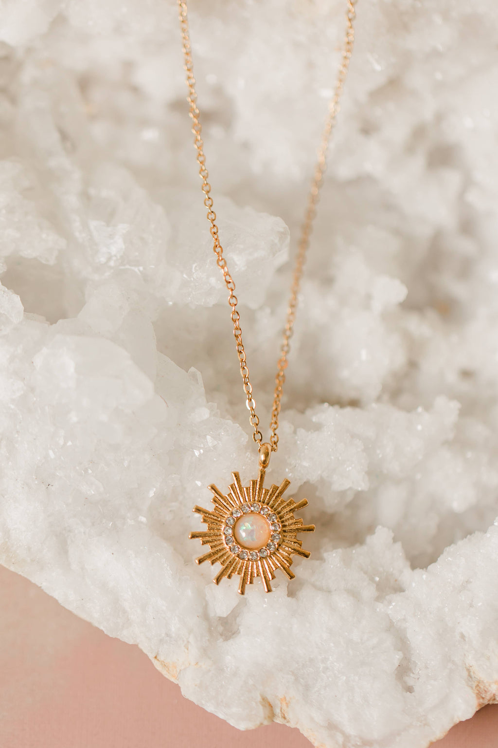 Gold sun-shaped necklace on a textured white surface