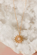 Gold sun-shaped necklace on a textured white surface