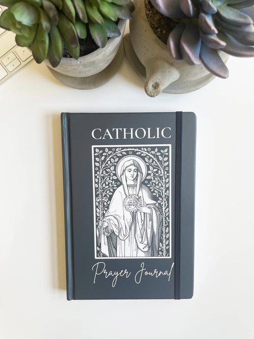 Catholic prayer journal with a decorative cover on a white surface with plants.