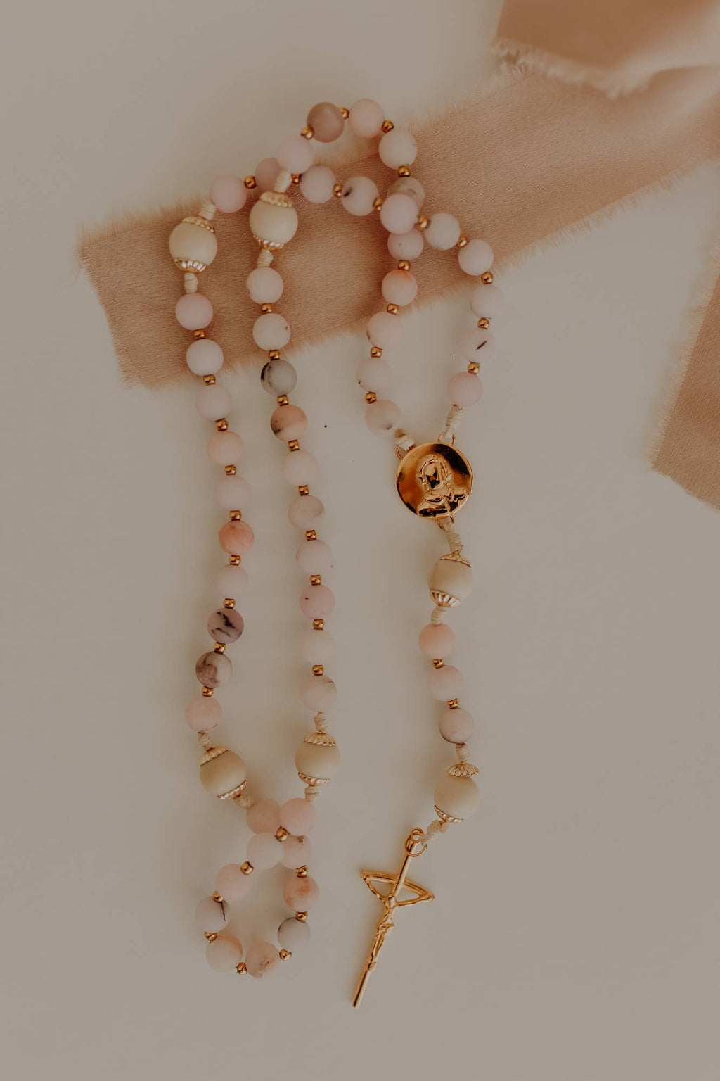 Catholic rosary with pink beads and a gold pendant and crucifix on a neutral background