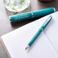 Teal pen and pen holder with motivational Bible quote on a notebook