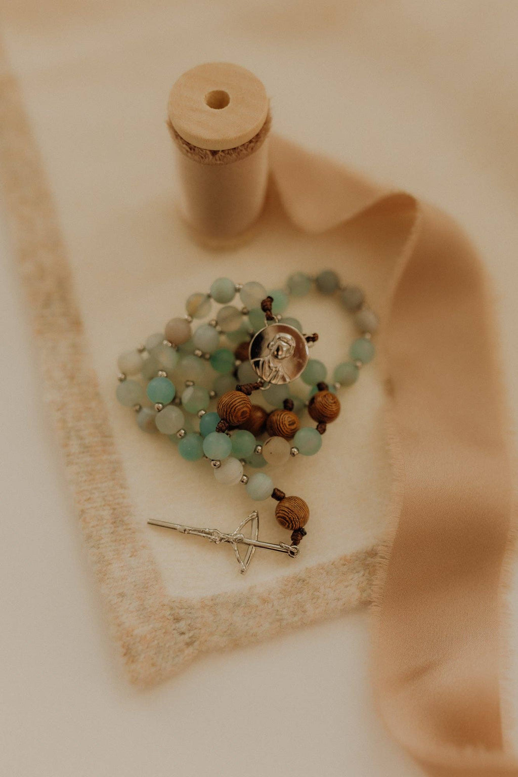 Catholic rosary with turquoise and brown beads and a silver crucifix on a beige fabric background
