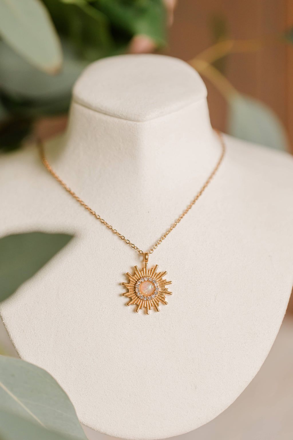 Gold necklace with a pendant on a mannequin bust with green leaves in the background