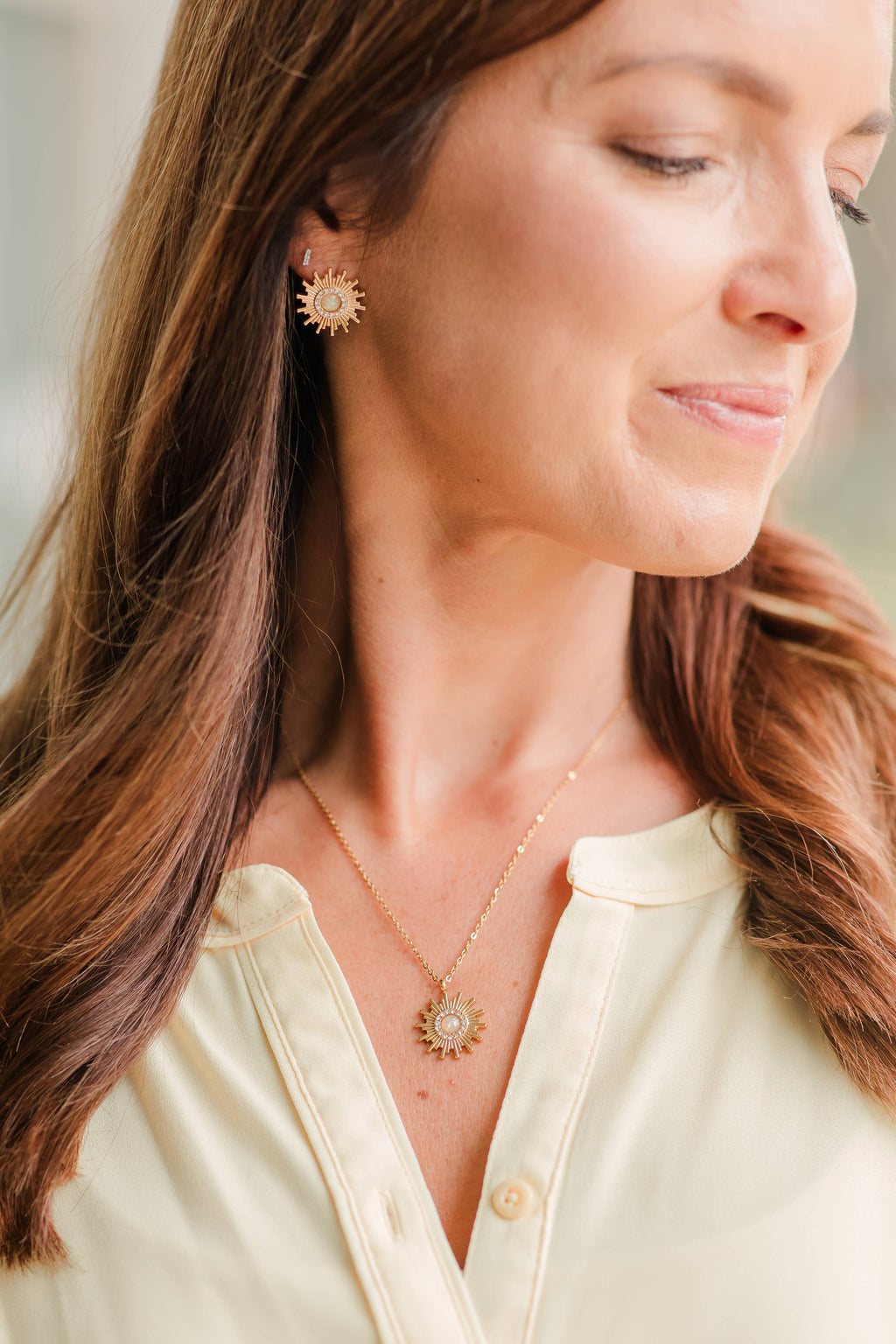Woman wearing sun-shaped earrings and a matching necklace with a blurred background