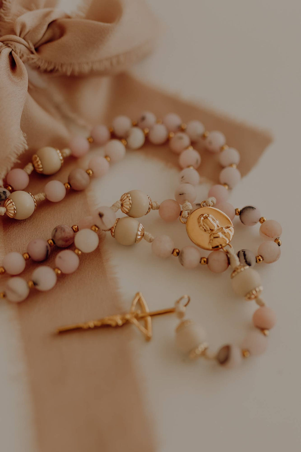 Catholic rosary with pink beads and a gold pendant and crucifix on a fabric background