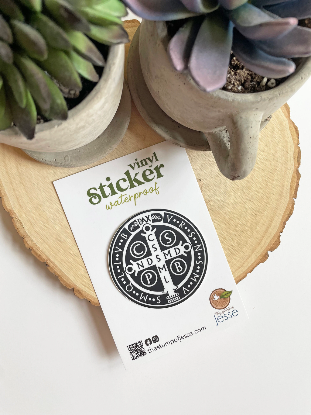 St. Benedict Medal Waterproof Sticker on a white card with plants in the background