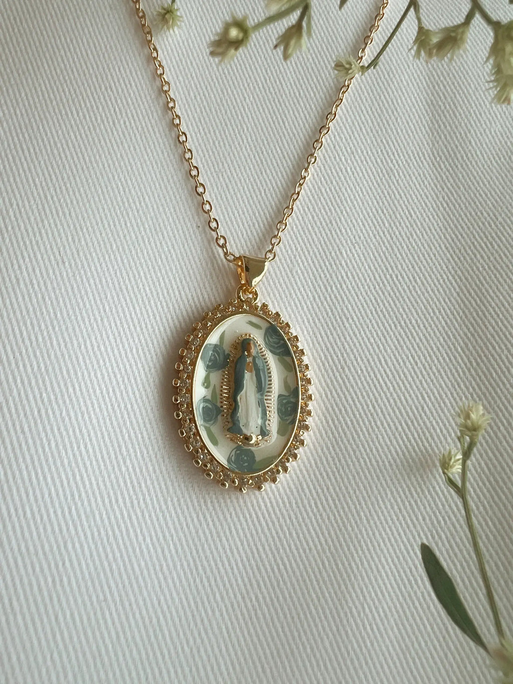 Gold necklace with a pendant featuring a religious design on a light background