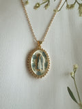 Gold necklace with a pendant featuring a religious design on a light background